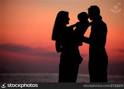 Silhouettes of parents with child on hands against sea decline