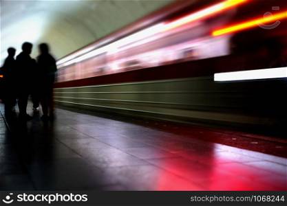 Silhouettes of people standing on the platform while a train is arriving. Subway train in blur.