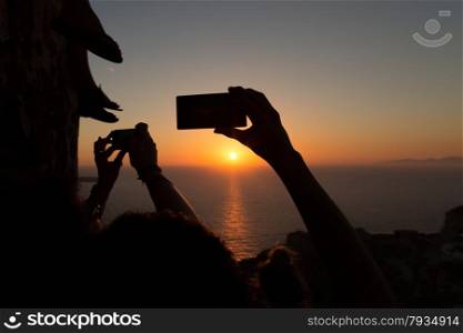 Silhouettes of people taking sunsets pictures with their smartphones