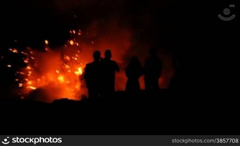 Silhouettes of sightseers in front of exploding lava at an active volcano in Hawaii