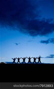 Silhouettes of six children standing together at the blue sky. Arms raised