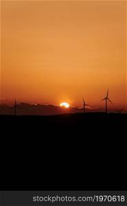 Silhouettes of some wind mills on the top of a mountain during a super orange sunset with copy space peaceful