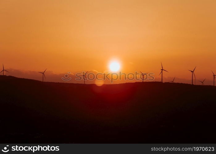 Silhouettes of some wind mills on the top of a mountain during a super orange sunset with copy space peaceful