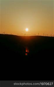 Silhouettes of some wind mills on the top of a mountain during a super orange sunset with copy space peaceful