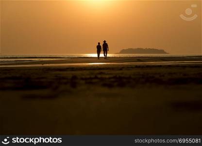 Silhouettes of tourists that are walking along the beach during sunset .