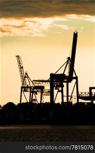 Silhouettes of two motionless, erect, idle harbor cranes against the setting sun