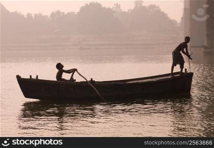 Silhouettes of two young males on boat, Ganges, Varanasi, India