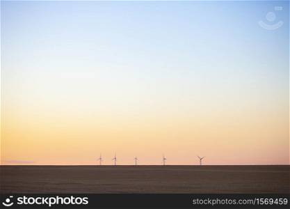 silhouettes of wind turbines behind empty fields in the north of france during colourful sunset