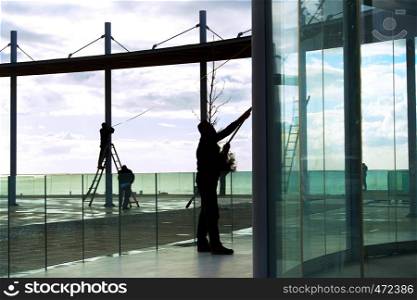 Silhouettes of workers cleaning glass constructions at modern viewpoint, Paphos, Cyprus