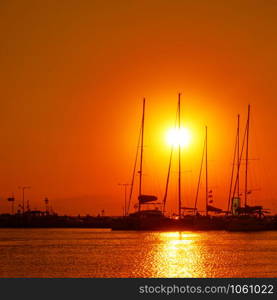 Silhouettes of yachts with tall masts at sunset at the port of Aegina, Saronic Islands, Greece