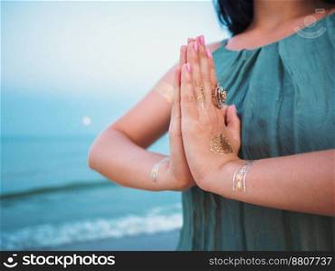 Silver and golden flash tattoo on female hands over sea or ocean background. Silver and golden flash tattoo on female hands over sea or ocean background. Woman practicing yoga. Namaste