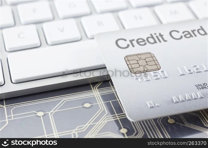 Silver credit card close up with selective focus on embossed numbers, electronic chip, modern white keyboard and digital circuits on background. Payment, online shopping, security financial concepts.