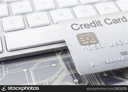 Silver credit card close up with selective focus on embossed numbers, electronic chip, modern white keyboard and digital circuits on background. Payment, online shopping, security financial concepts.