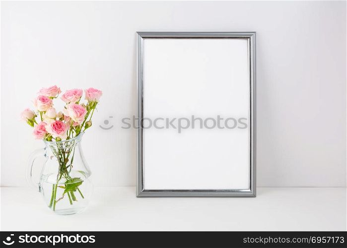 Silver frame mockup with pink roses. Portrait or poster white frame mockup. Empty white frame mockup for presentation artwork.. Silver frame mockup with pink roses