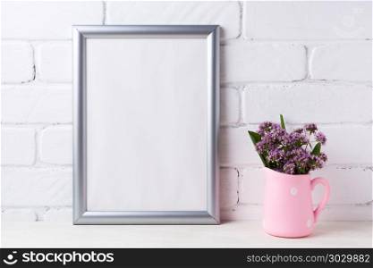 Silver frame mockup with purple flowers in pink rustic pitcher . Silver frame mockup with purple field flowers in polka dot pink rustic pitcher vase. Empty frame mock up for presentation artwork. Template framing for modern art.