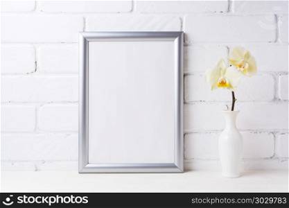 Silver frame mockup with soft yellow orchid in vase. Empty frame mock up for presentation artwork. Template framing for modern art.. Silver frame mockup with soft yellow orchid in vase