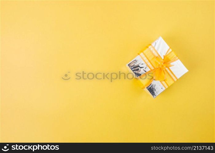 silver gift box decorated with yellow ribbon yellow background