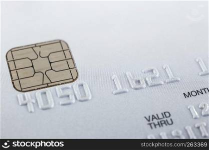 Silver gray smart credit card, PVC EMV, close up with selective focus on embossed numbers, electronic chip, dots pattern on background and white blank copy space on top. Payment, security financial.