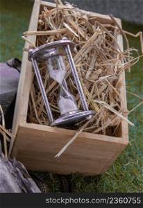 Silver hourglass or Sandglass on straw background in wooden box. Gift concept of good moments, Dark tone, Selective focus.