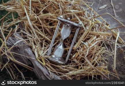 Silver hourglass or Sandglass on straw background. Past moments concept, Selective focus.