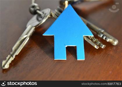 Silver key with blue house figure on wooden background