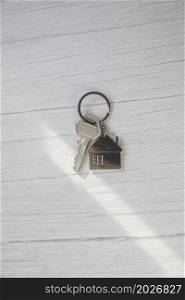 Silver key with silver house figure on white wooden background, buying new house real estate concept copy space top view. Silver key with silver house figure on white wooden background, buying new house real estate concept copy space