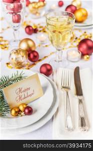Silver knife and fork, christmas ball and green spruce branche lie on the white porcelain plate, glass of wine, which is located on a table covered with a white tablecloth