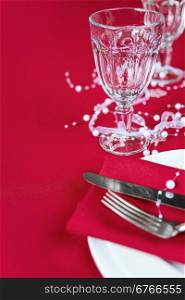 Silver knife and fork lie on the red linen napkin, as well as wineglass, which is located on a table covered with a red tablecloth, with space for text