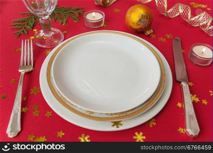 Silver knife, fork, dinner plates, wineglass and burning candles, which is located on a table covered with a red tablecloth