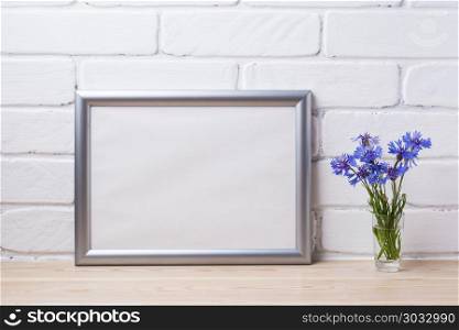 Silver landscape frame mockup with cornflower. Silver landscape frame mockup with blue cornflower in the simple glass vase. Empty frame mock up for presentation artwork. Template framing for modern art.