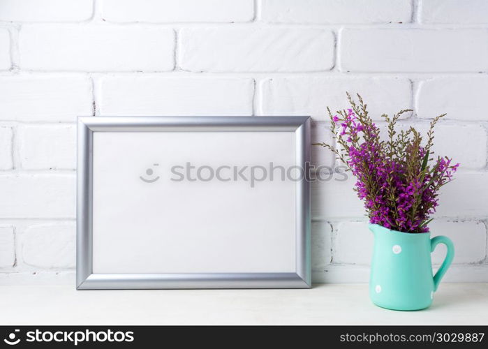 Silver landscape frame mockup with maroon purple flowers in mint. Silver landscape frame mockup with maroon purple field flowers in polka dot mint green pitcher vase. Empty frame mock up for presentation artwork. Template framing for modern art.