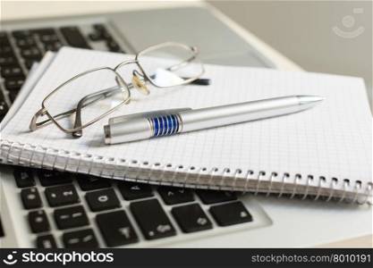 silver laptop computer with notepad, pen, glasses and keyboard