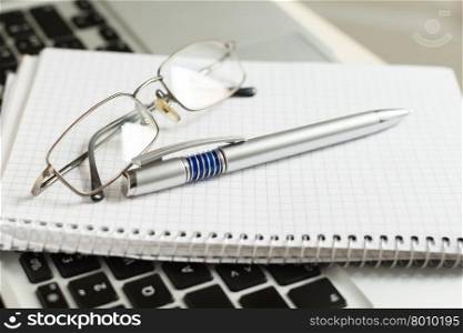 silver laptop computer with notepad, pen, glasses and keyboard