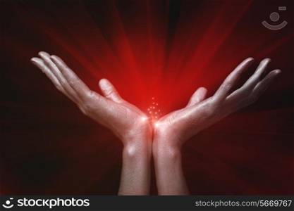 Silver men&rsquo;s hands holding red magic glow on black background