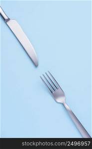 Silver metal knife and fork creative flat lay on soft blue trendy pastel background
