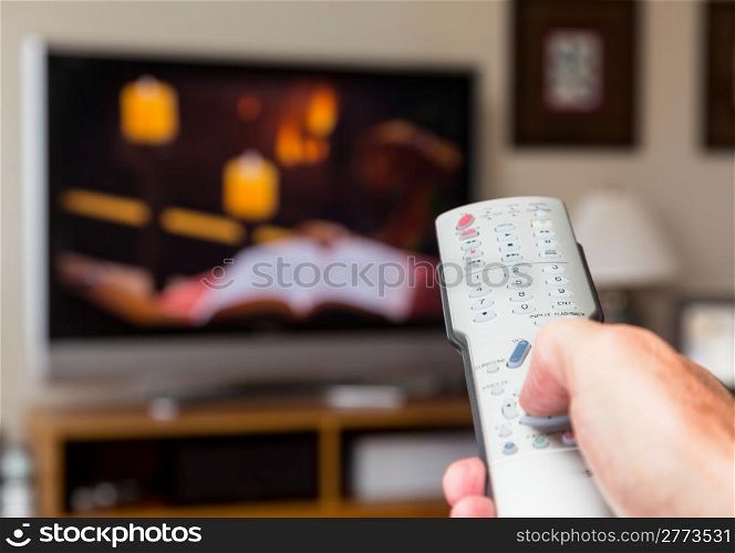 Silver modern TV remote control being pressed by thumb with out of focus screen background