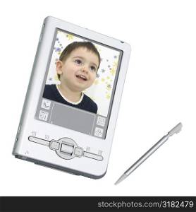 Silver palmtop (personal organizer) / digital camera over white. Screen shows happy toddler boy with winter snowflakes in yellow and blue in background.