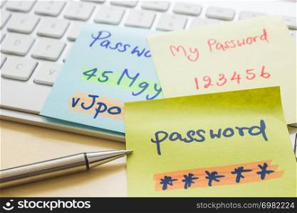 Silver pen pointing at handwriting passwords with highlight colors written on paper notes at modern white keyboard with office table on background. Data privacy management and cyber security concepts.