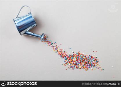 silver watering can pouring sugar baking colorful sprinkles in shape of circle on a light beige background.. silver watering can pouring sugar baking colorful sprinkles in shape of circle on light beige background.