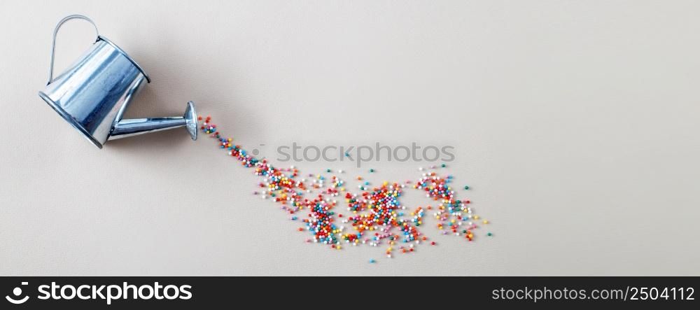 silver watering can pouring sugar baking colorful sprinkles in shape of circle on a light beige background. banner. silver watering can pouring sugar baking colorful sprinkles in shape of circle on light beige background. banner