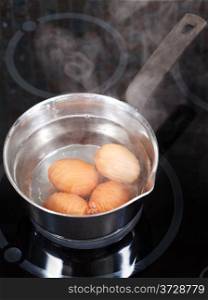 simmering chicken eggs in metal pot on electric stove in kitchen