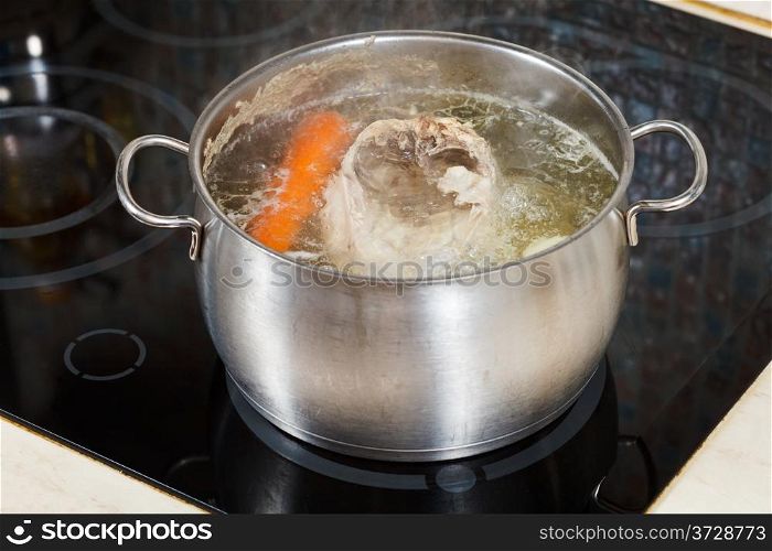 simmering chicken soup with seasoning vegetables in steel pot on glass ceramic cooker