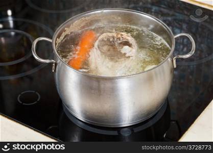simmering chicken soup with seasoning vegetables in steel pot on glass ceramic cooker