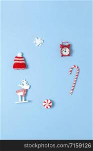 Simple creative Christmas composition. Candy cane, deer, hat, snowflake, red clock on blue background, copy space. Minimal style. Top view. Vertical. For social media, greeting card, office supplies.