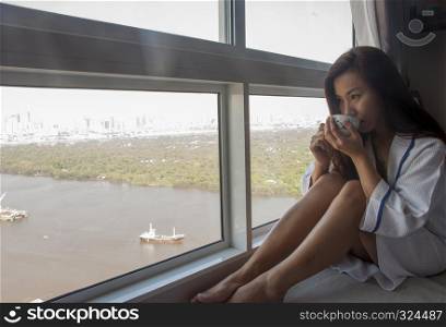 Simple lifestyle. Asian women wake up in the morning and relax with a cup of coffee in a city room.