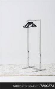 Simple metal clothing rail with empty coat hangers. Simple metal clothing rail with empty coat hangers standing at an angle on a long pile white rug in a white room with copyspace on the wall