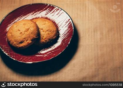 Simple top view of round crunchy sweet cookies with candied fruit, on red saucer, baking paper background