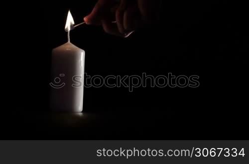 Simple white candle burning on black background with copy space for something.