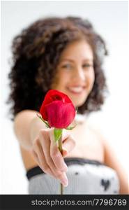 Sincere beautiful young woman with brown curly wild hair and bare shoulders presenting red rose, isolated