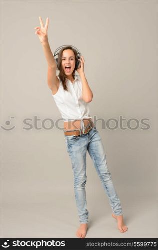 Singing teenage girl headphones show victory sign full length on gray